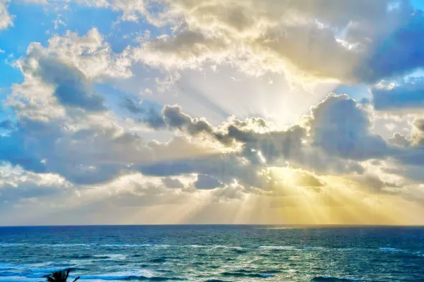 Ocean view with radiant sunlight breaking through clouds, symbolizing divine love and spiritual awakening.