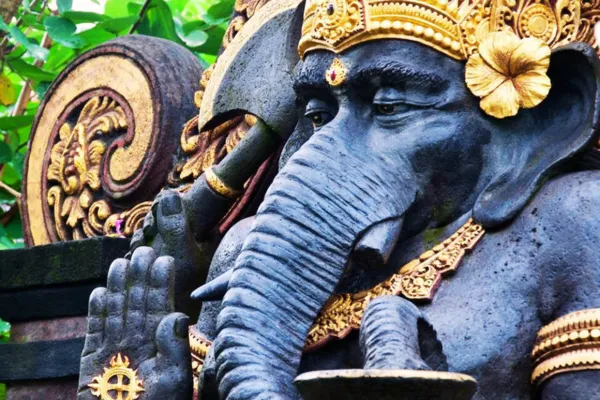 Elephant deity statue adorned with gold accents, symbolizing divine love and spiritual wisdom, set against a lush green background.