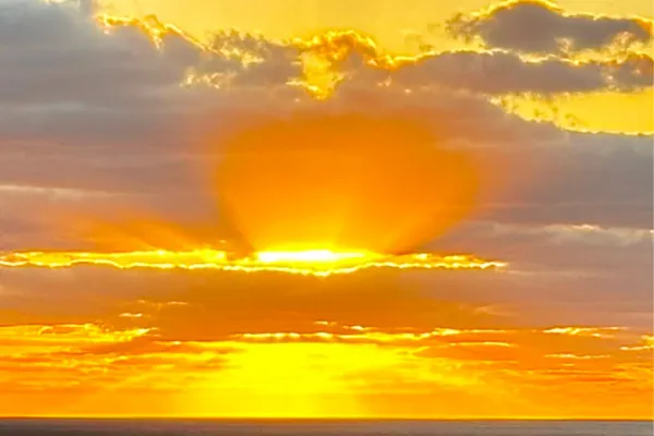 Sunrise over the ocean with vibrant orange and yellow hues illuminating the clouds, symbolizing divine love and spiritual awakening.